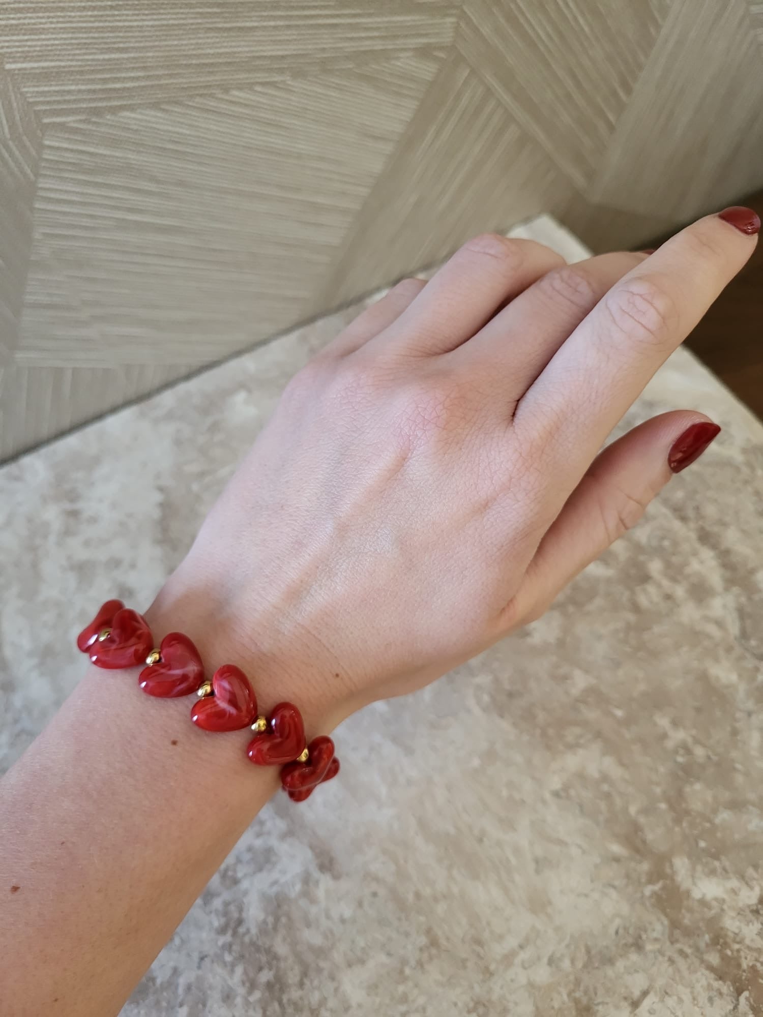 Rode hartjes armband van roestvrij staal om een vrouwenpols met rode nagellak