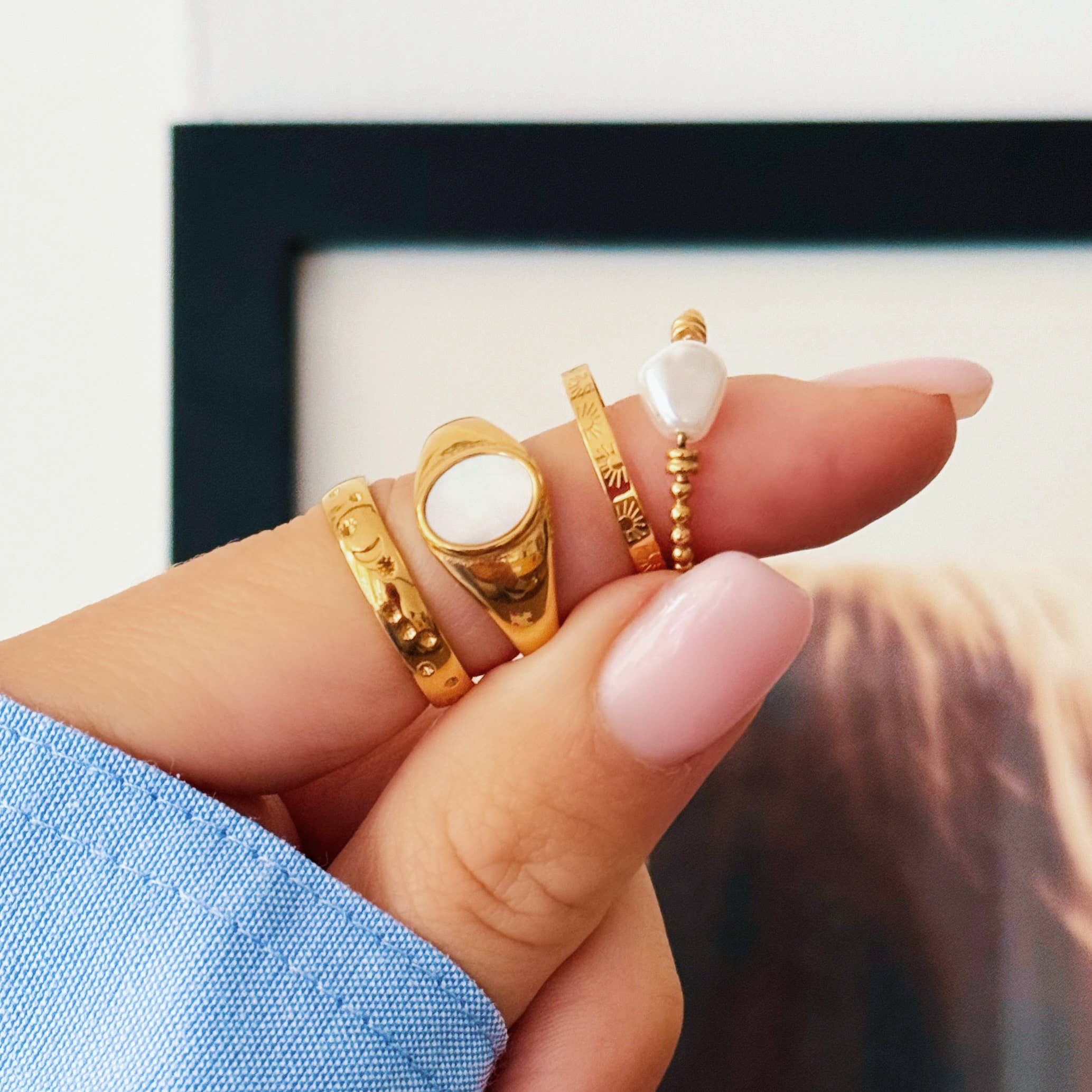 Hand met gouden roestvrijstalen ringen, waaronder een Pearl Bead ring, een zegelring en graveerde ringen.