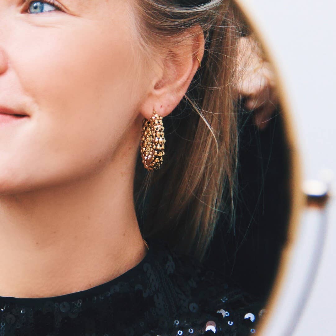 Vrouw met gouden Party Hoops oorbellen van stainless steel, draagt zwarte top met pailletten, feestelijke sieraden.