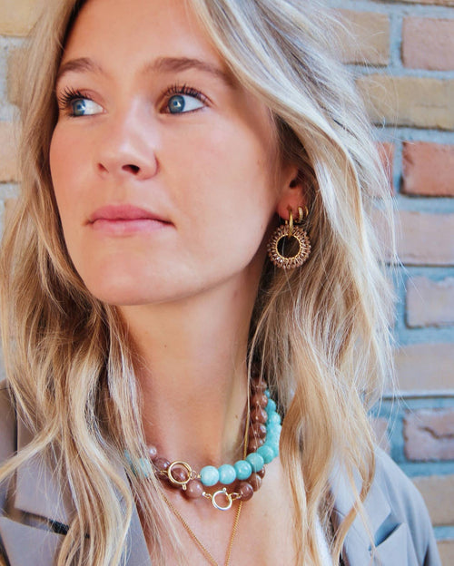 Vrouw draagt Bloom Circle oorbellen van stainless steel met gouden afwerking, naast turkoois en bruine kettingen.