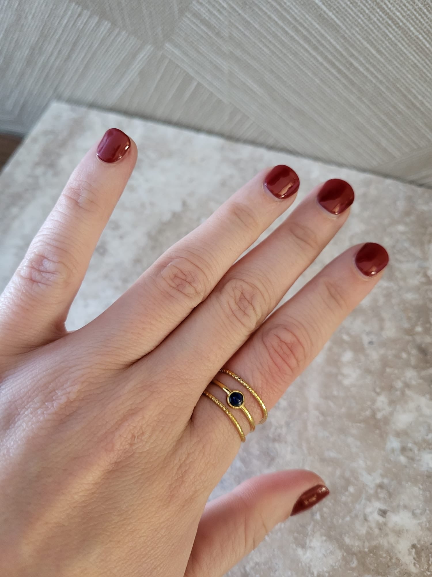 Drie blauw-gouden ringen met natuursteen, gedragen om een vinger met rode nagellak. Verfijnde stainless steel sieraden.