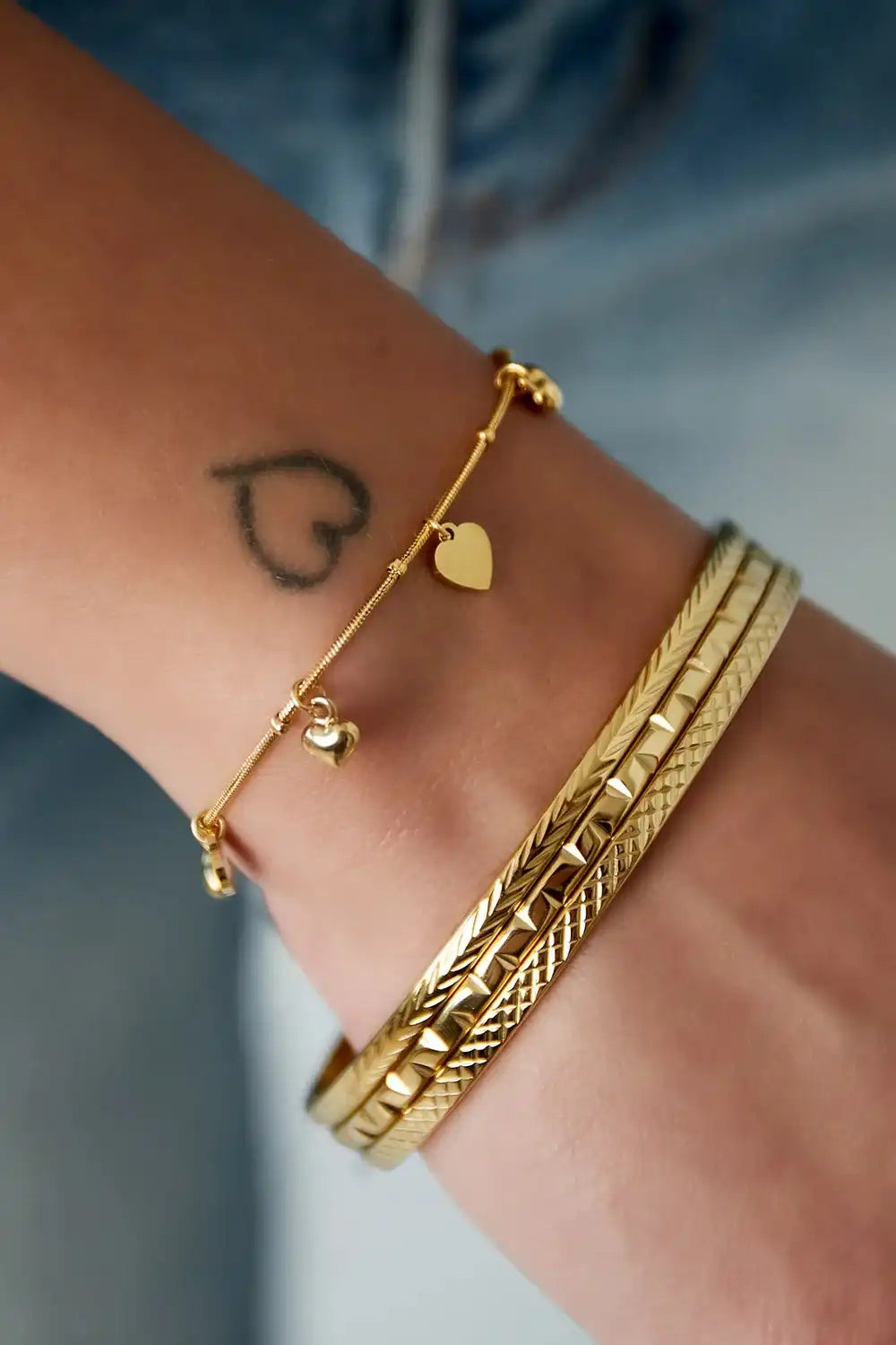 Gouden schakel armband met hartjes bedels en slanke gouden armbanden om de pols, van stainless steel.