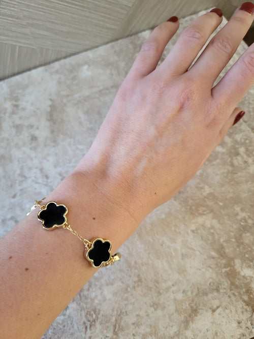 Gouden edelstalen armband met zwarte bloem vormige bedels op een vrouwenarm, Belle collectie