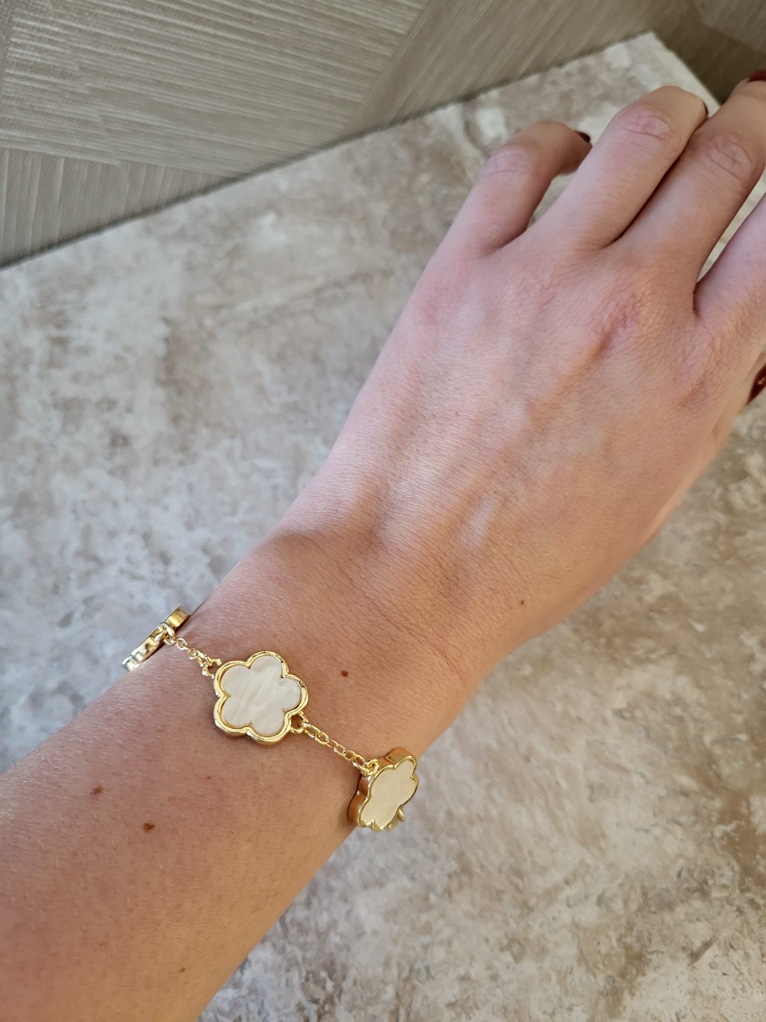Gouden Belle armband van roestvrij staal met witte klaverhanger, gedragen om de pols.