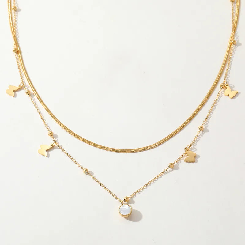 Gouden dubbele ketting van roestvrij staal met vlinder bedeltjes en een ronde schelpmotief hanger.