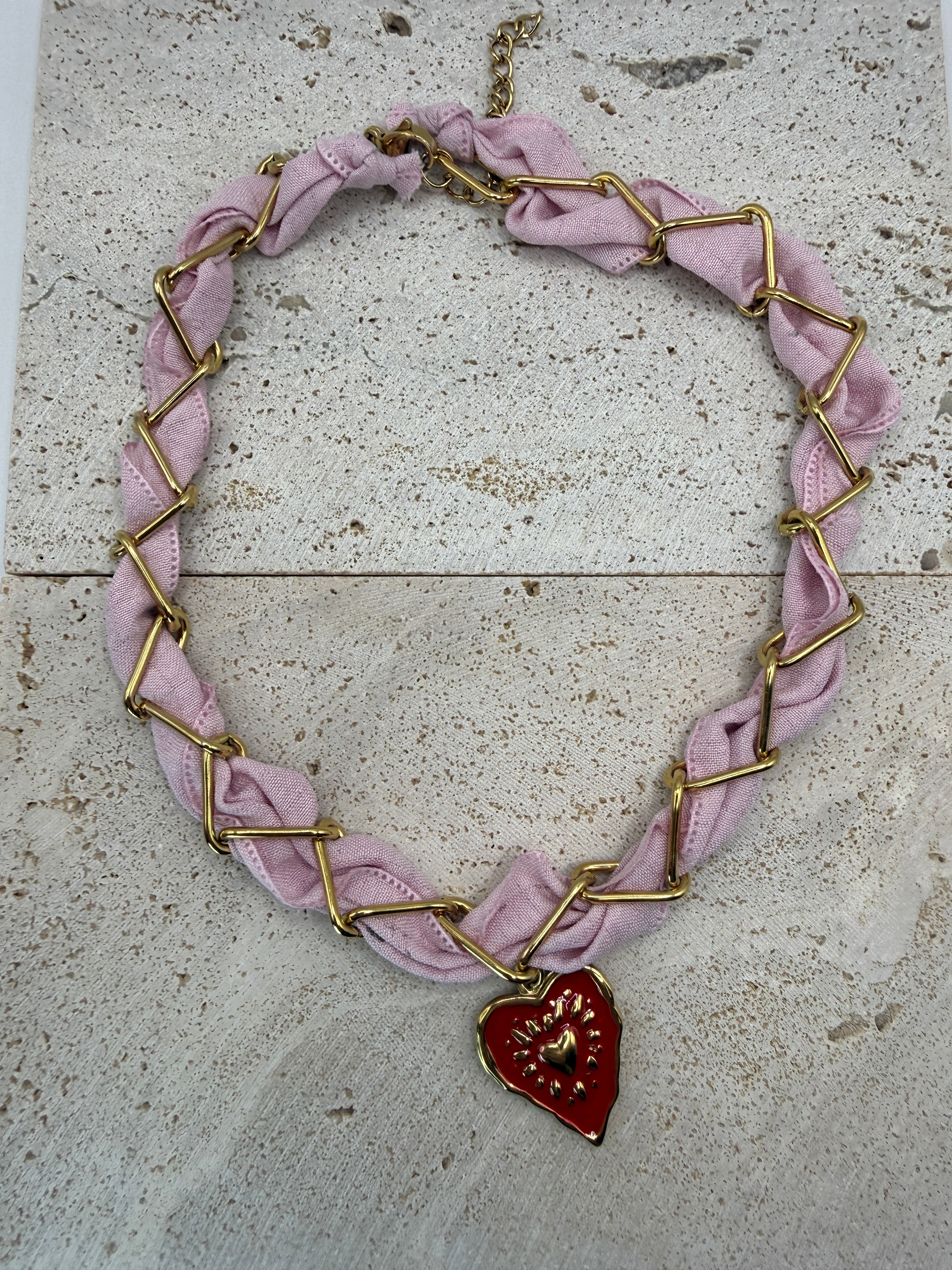 Celeste pink roestvrijstalen ketting met gouden schakels, verweven met roze stof en een rood hartje hanger