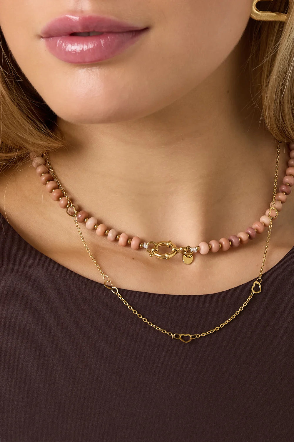 Model draagt roze kralenketting van natuursteen met gouden front clasp en een gelaagde gouden ketting