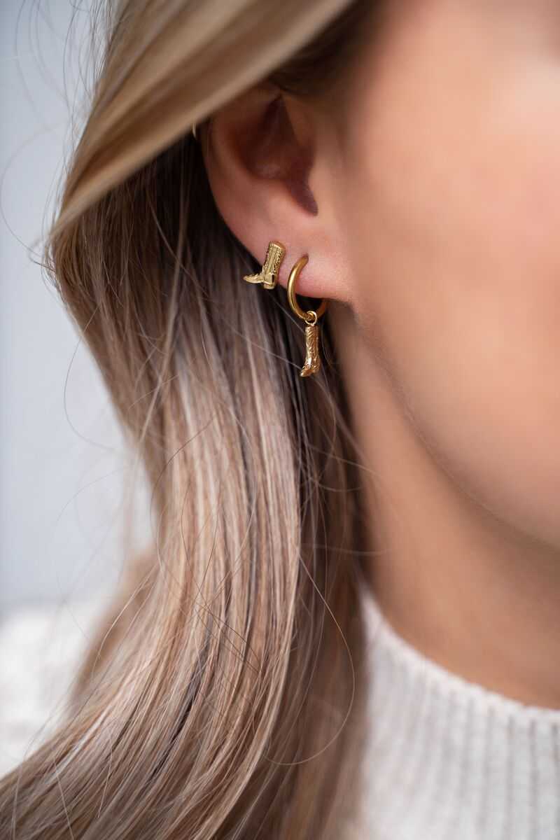 Gouden cowboylaars oorbellen hoepel en stud van stainless steel op het oor van een blond model
