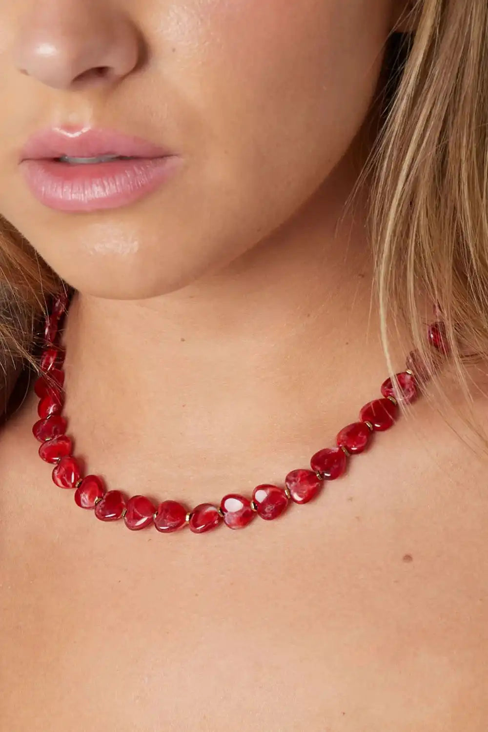 Close-up van vrouw met een rode kralen ketting van glanzende, hartvormige kraaltjes, trendy roestvrijstalen sieraden