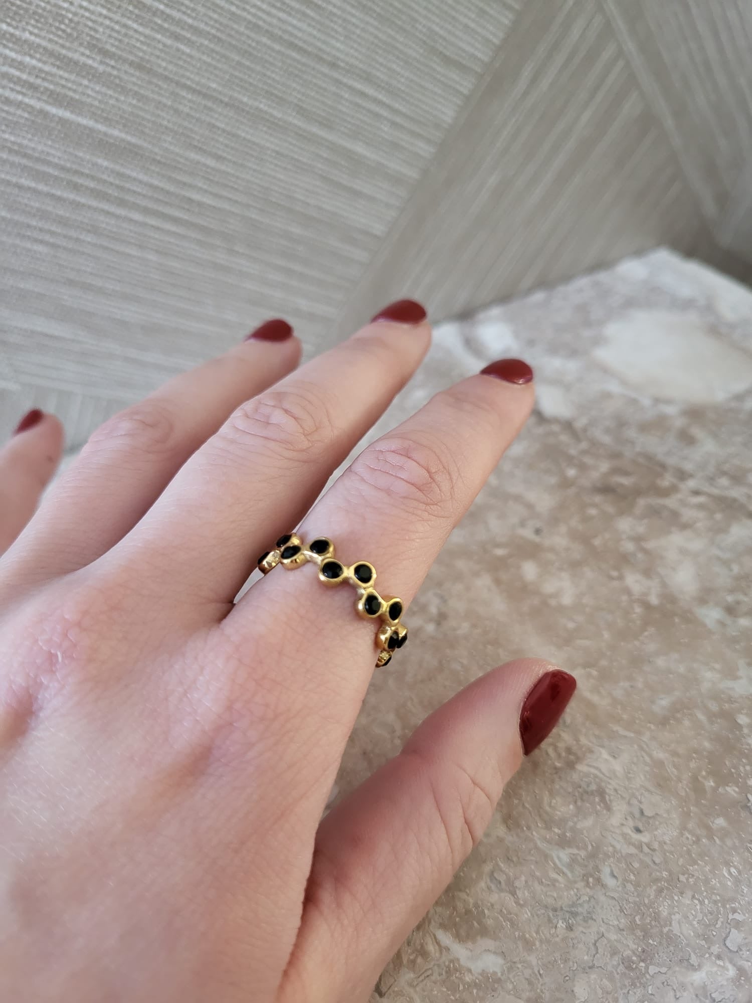 Gouden roestvrijstalen ring met golvend patroon en zwarte steentjes, gedragen op een vinger.