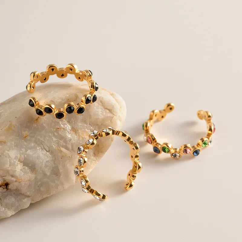Drie gouden roestvrijstalen Waves ringen met gekleurde, zwarte en transparante zirkonia steentjes op witte steen.