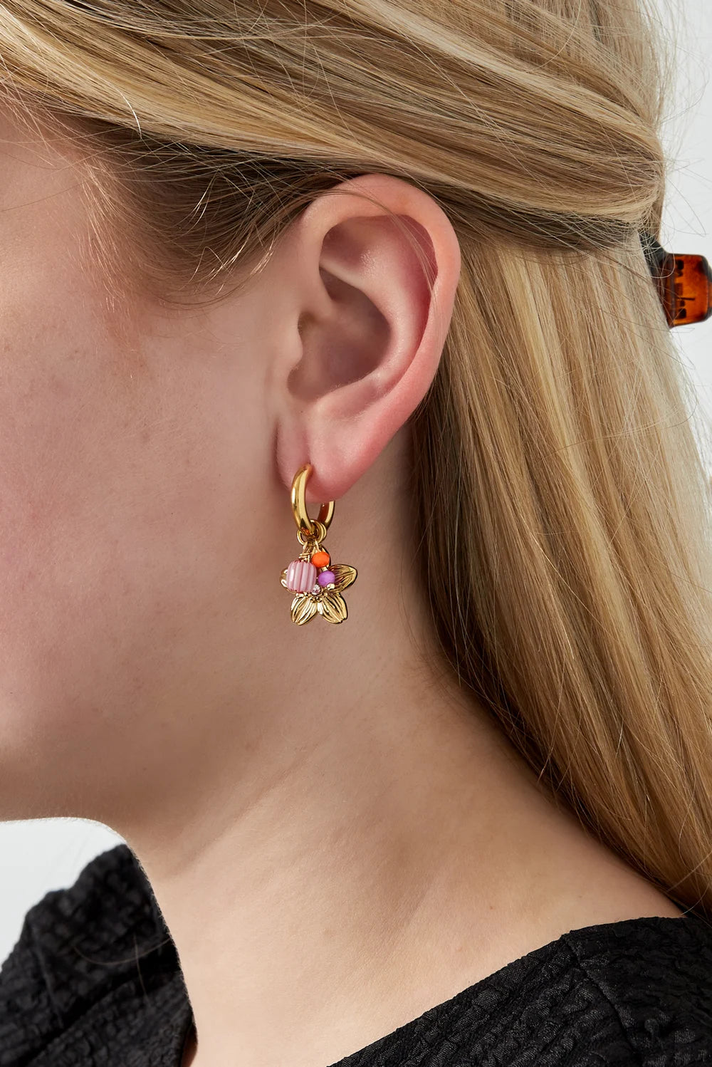 Gouden stainless steel oorbel met bloemhanger, roze en oranje kraaltjes gedragen door een vrouw