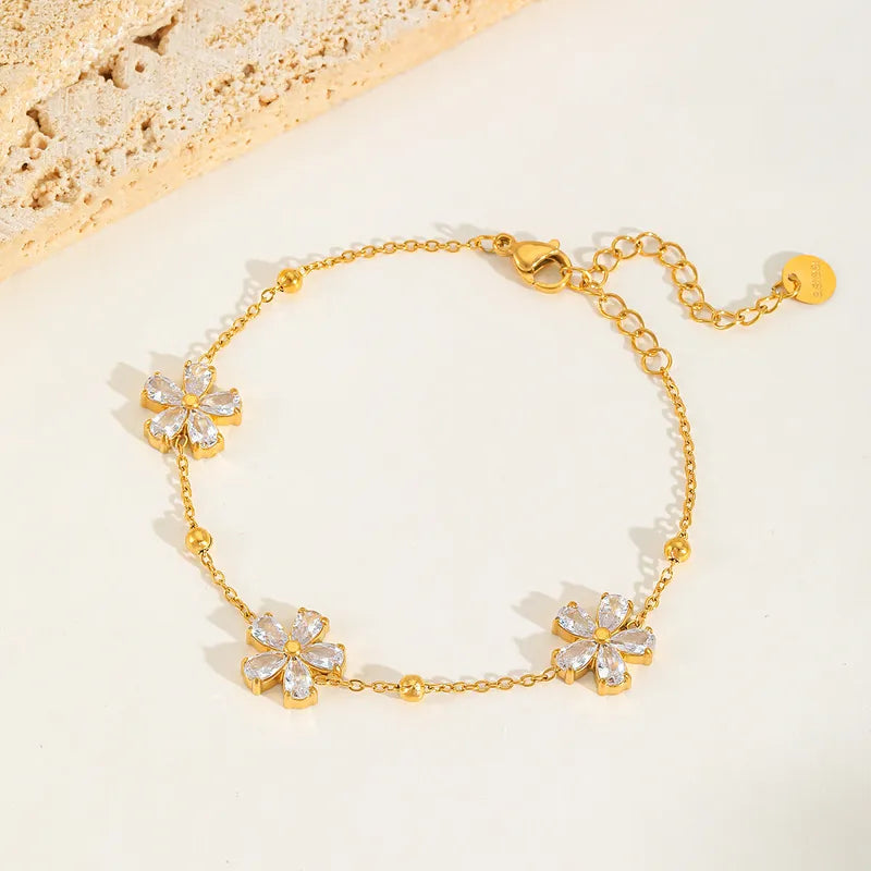 Goudkleurige stainless steel armband met drie glinsterende bloemmotieven en verstelbare sluiting. Sierlijke damesarmband.