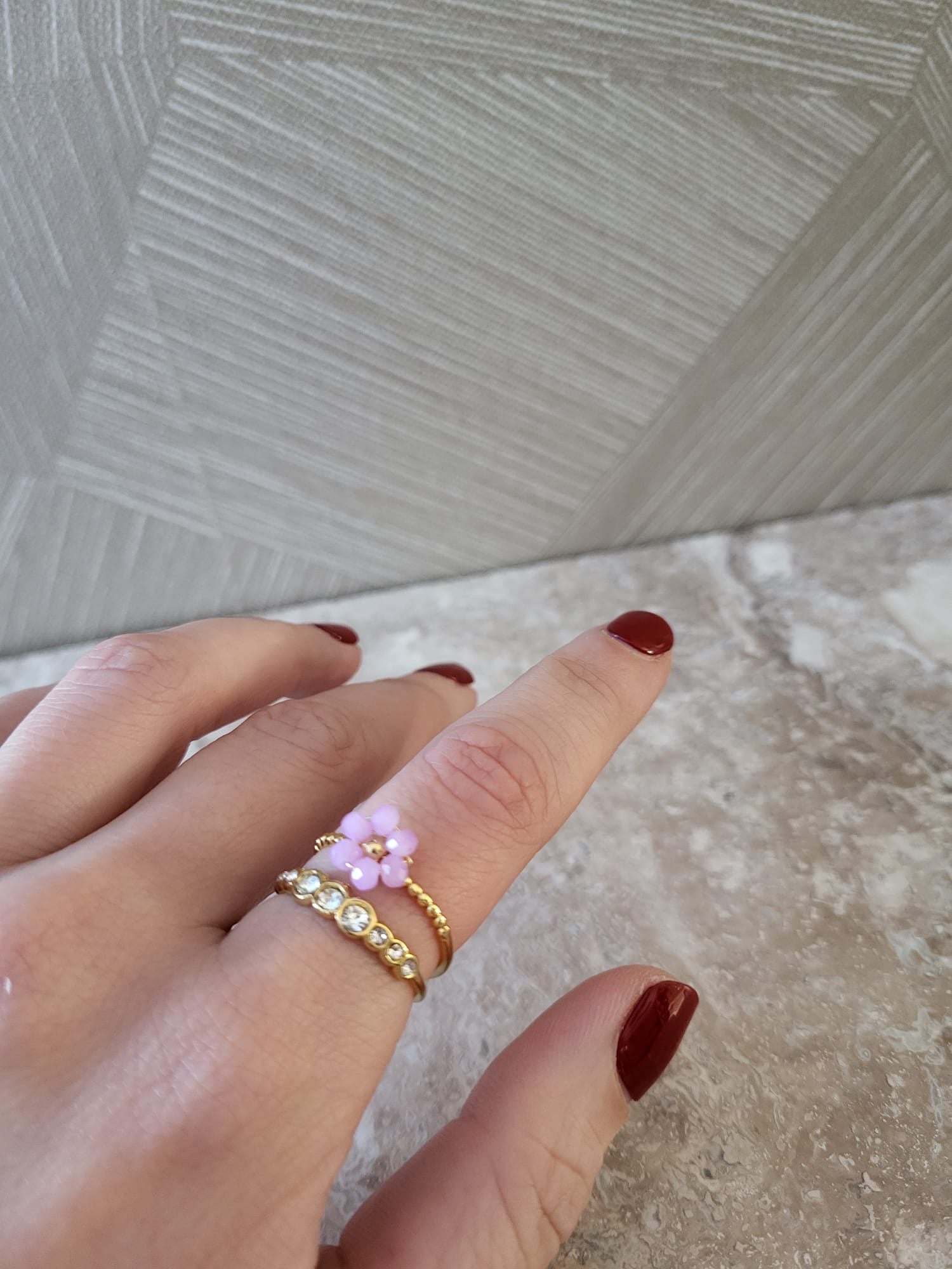 Vrouw draagt aan vinger gouden stainless steel ring met paars bloemetje en ring met witte steentjes erop.