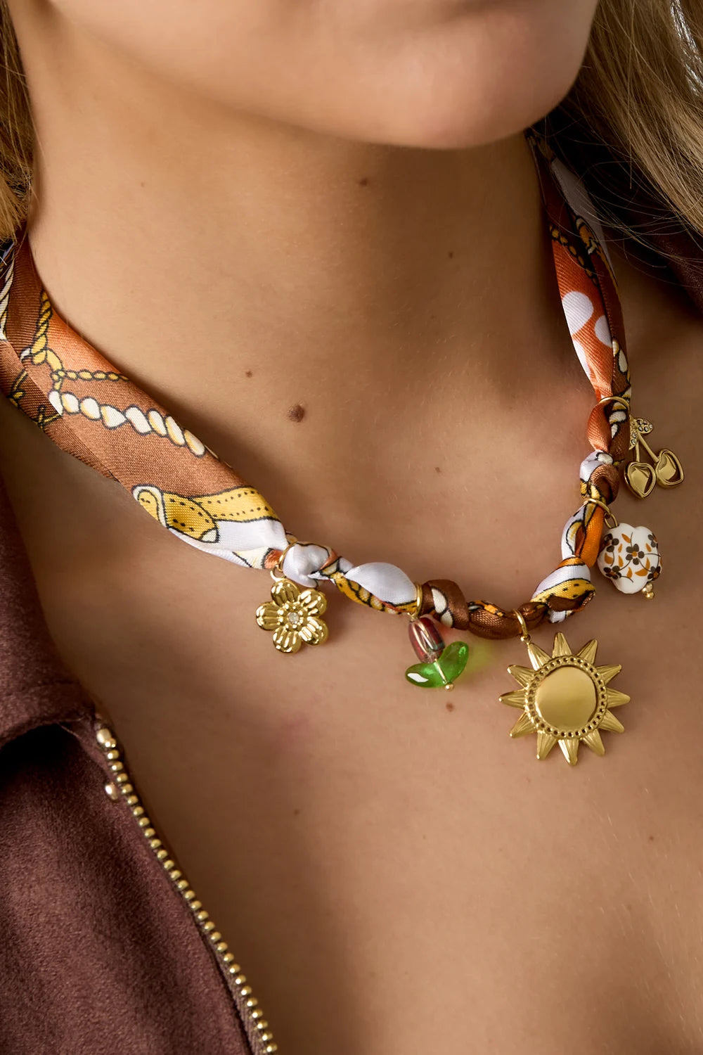 Multicolor statement ketting met gouden bedels van bloem, zon, hartjes en bladeren om de hals van een vrouw.