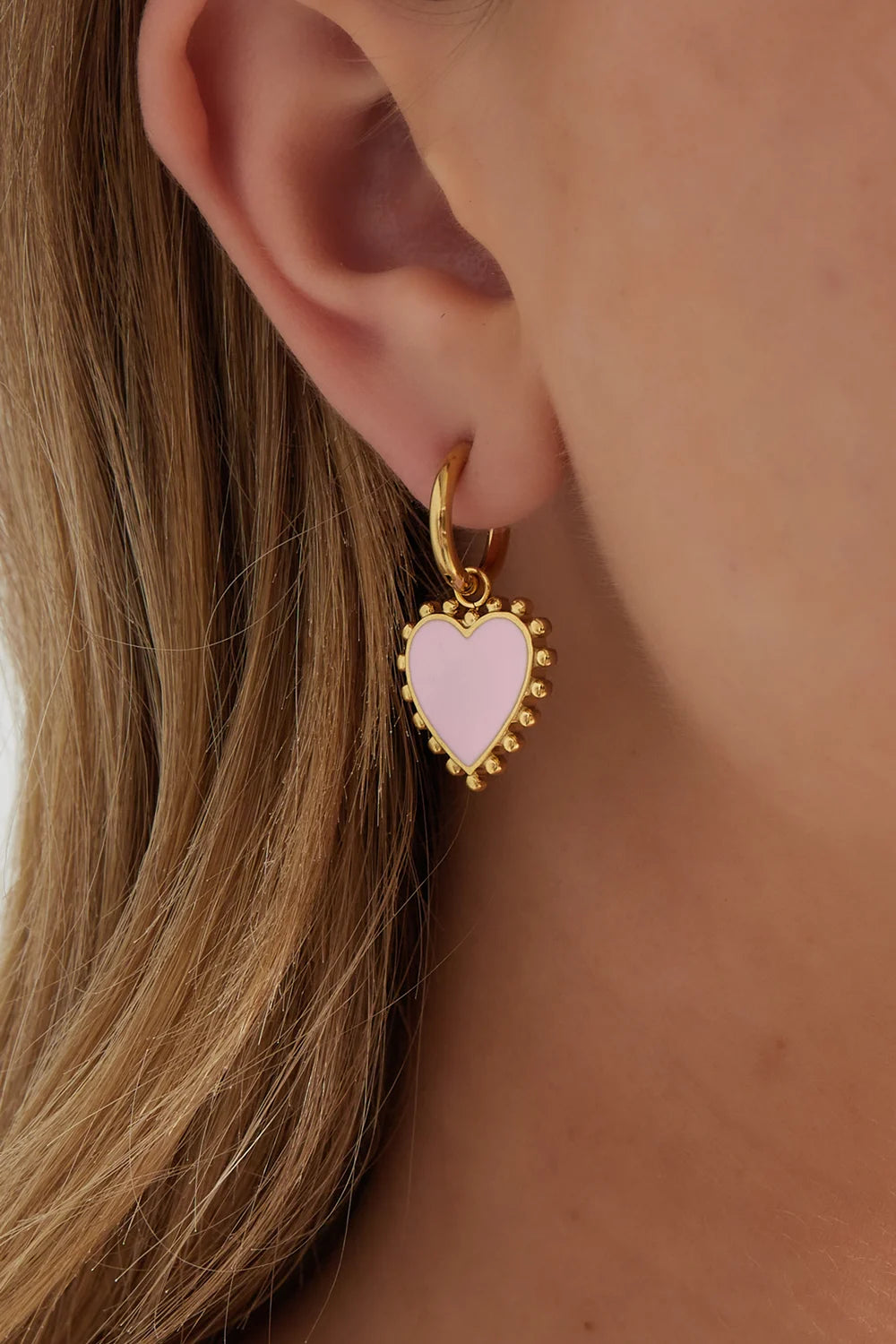 Gouden funky oorbellen van stainless steel met een roze hanger in de vorm van een hartje gedragen door een vrouw.