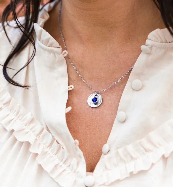 Zilveren ketting met ronde hanger en blauwe geboortesteen gedragen op een vrouw, elegant verjaardagscadeau