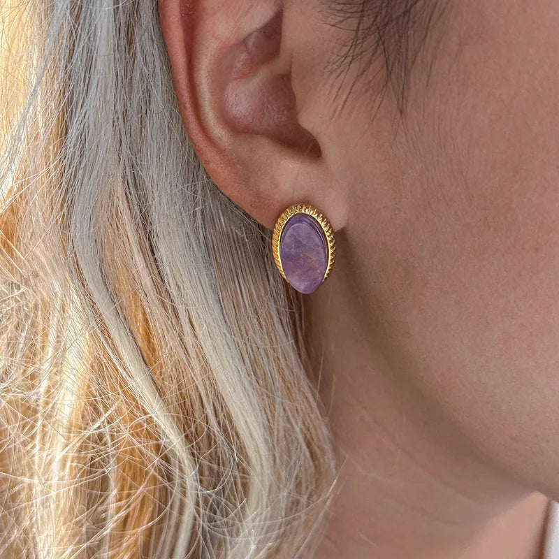 Oorbellen met ovale paarse natuursteen en gouden, geribbelde rand van stainless steel op de oorlel van een vrouw.