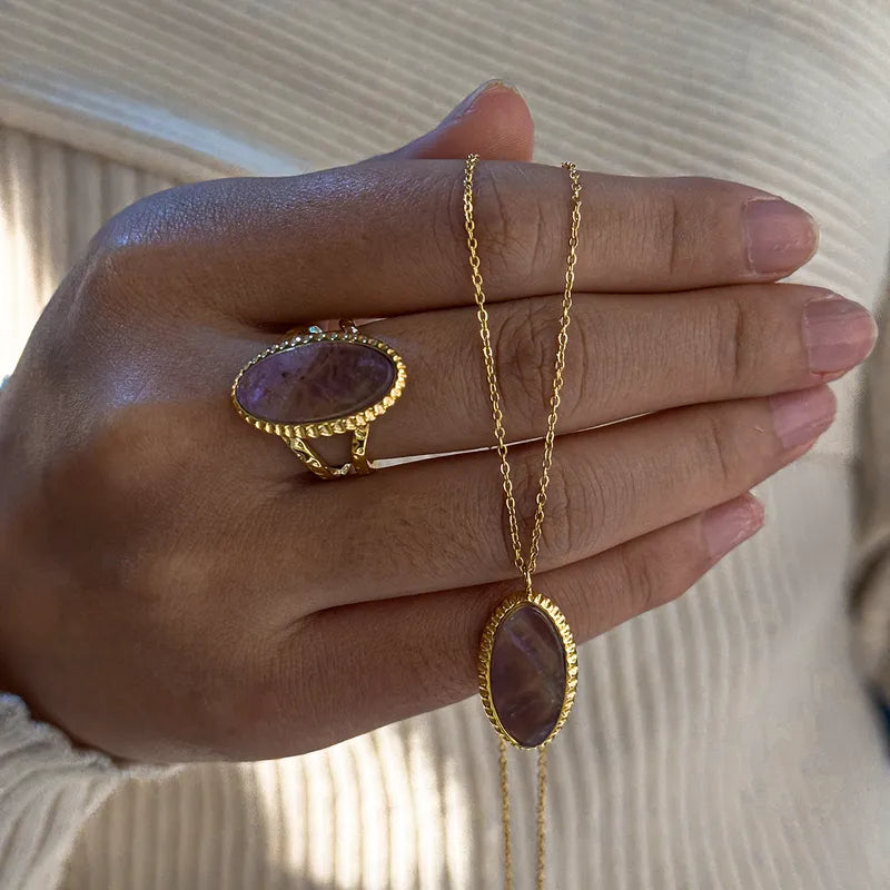 Gouden ketting en ring met ovale paarse natuursteen hanger en edelsteen in stainless steel op een hand.