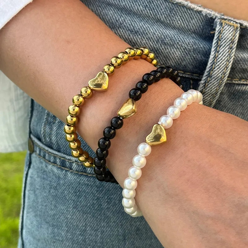 Drie gouden, zwarte en parelmoer-witte hartjes armbanden van stainless steel op de arm van een vrouw