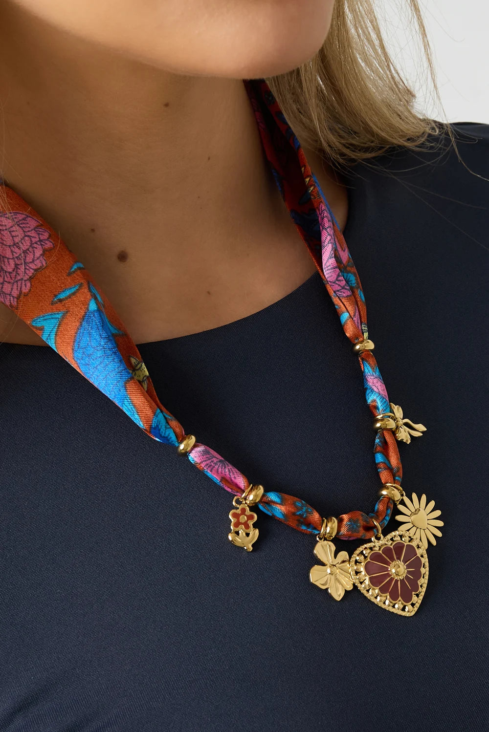 Close-up van een vrouw die een multicolor statement ketting draagt met een hart, bloemen en andere goudkleurige bedels.