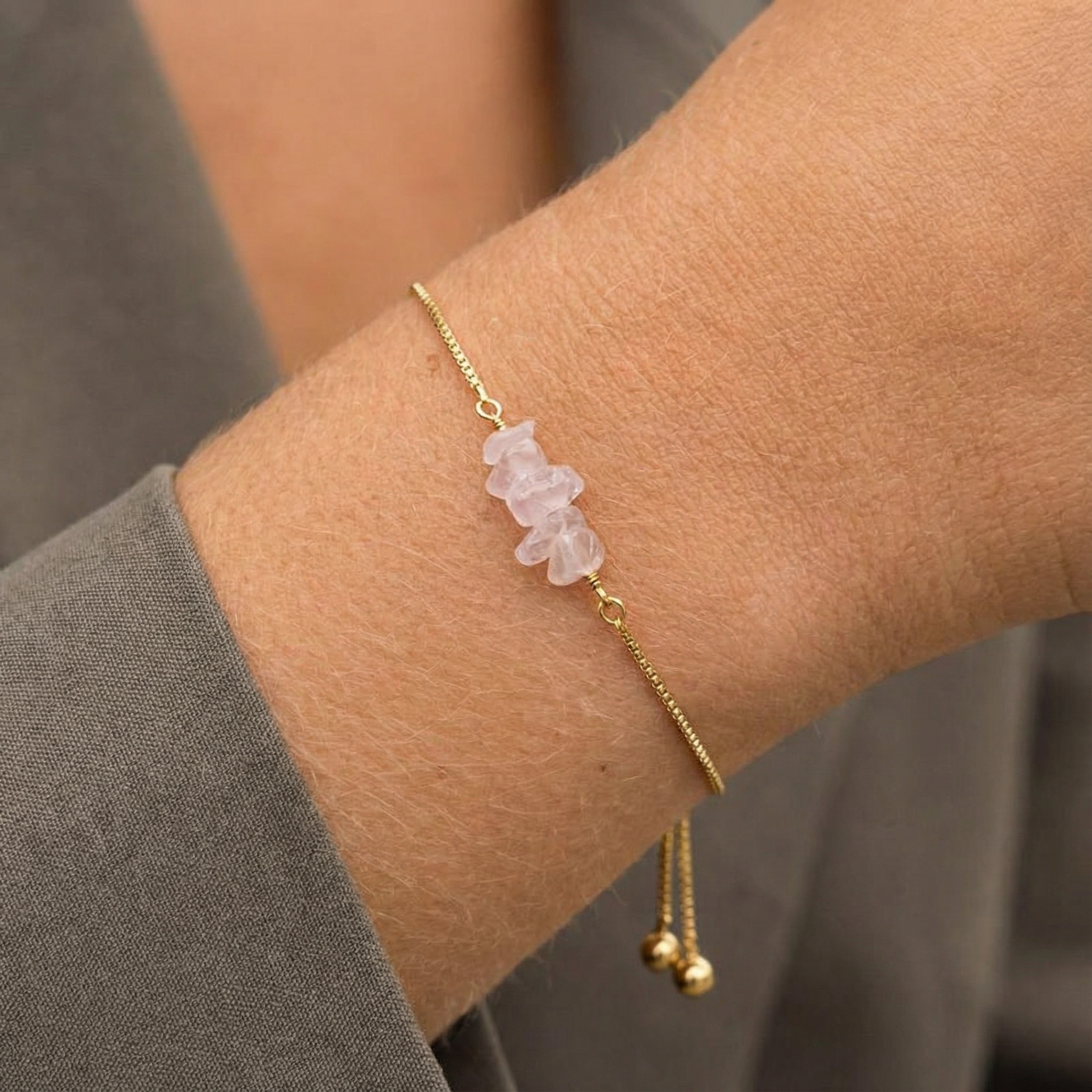 Gouden schakelarmband met onregelmatige, zachtroze rozenkwarts edelsteentjes om een pols, verstelbaar, sieraad