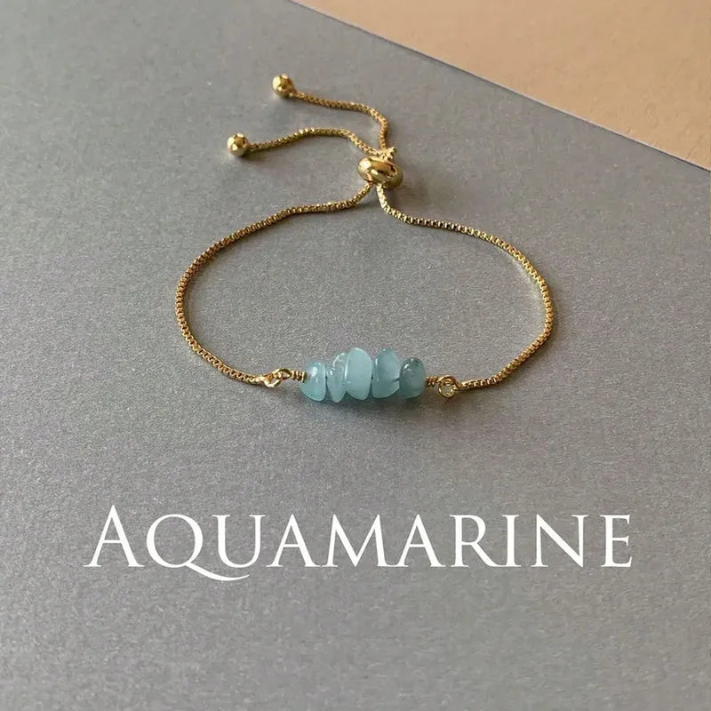 Goudkleurige verstelbare armband met vier ruwe, lichtblauwe aquamarijn natuursteen chips als eyecatcher, gedetailleerd close-up.