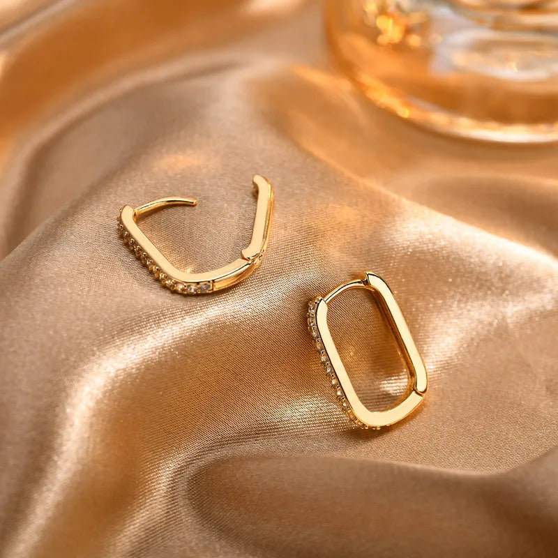 Goudkleurige sparkling oval hoops oorbellen van stainless steel met glinsterende zirkonia steentjes op satijnen ondergrond.