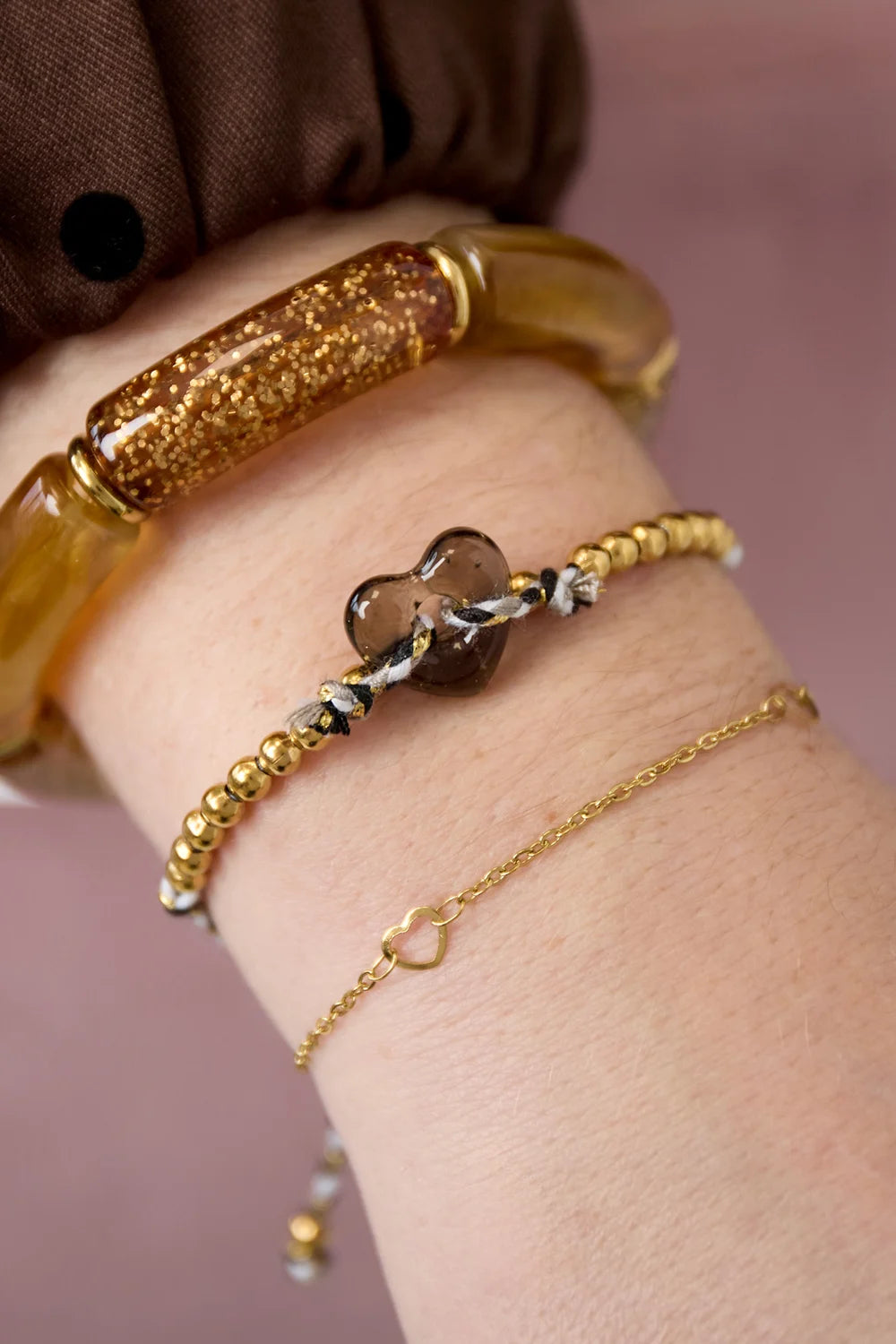 Jill hartjes armband lichtbruin met gouden kraaltjes om de pols gedragen, met gouden schakelarmbandje en glitterarmband.
