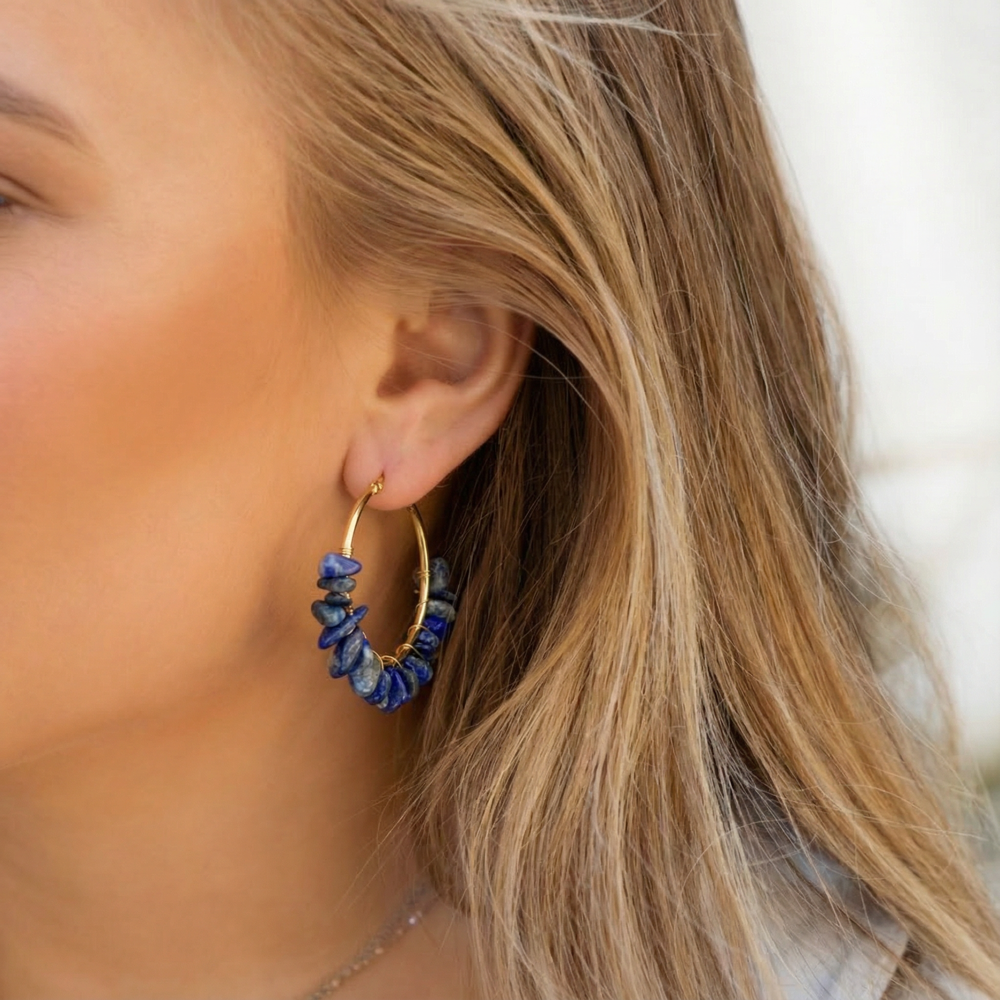 Vrouw met prachtige Lapis Lazuli oorbellen van natuursteen, grote gouden hoops met blauwe edelstenen, stainless steel sieraad