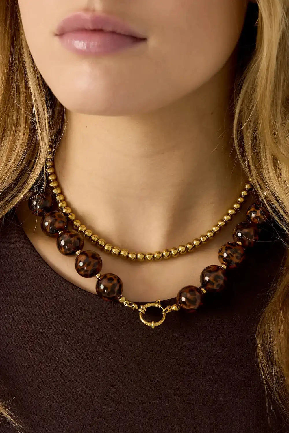 Gestapelde gouden kralenketting en leopard print kralenketting met gouden sluiting om hals vrouw