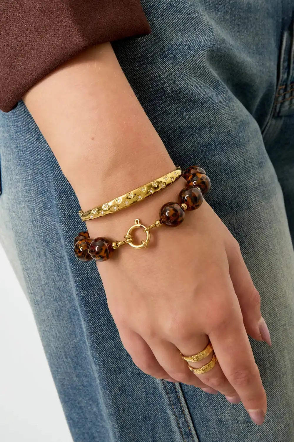 Vrouwenhand met goudkleurige stainless steel Leopard kralen armband en bijpassende gouden ringen, casual stijl.