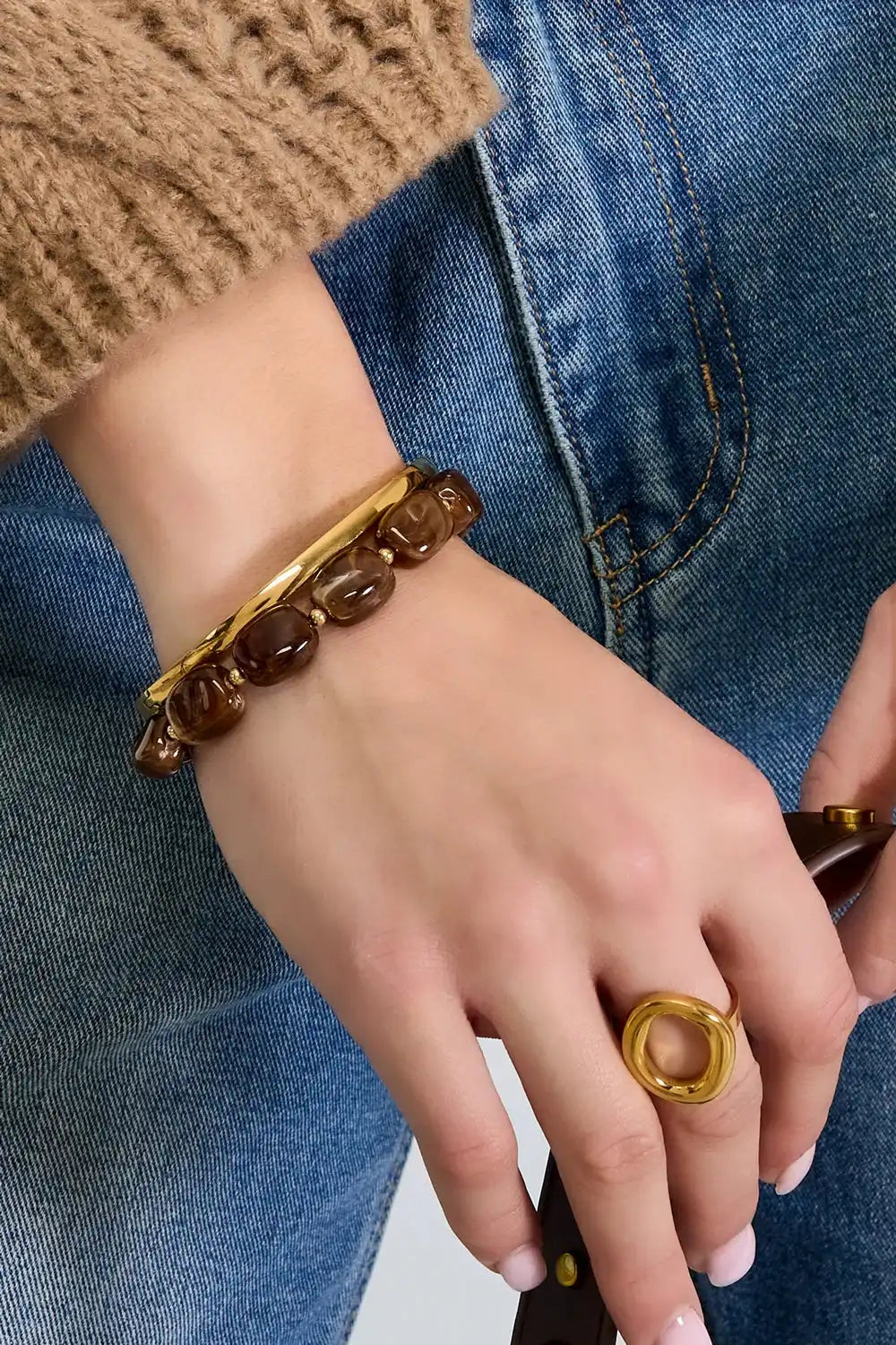 Ruby Red kralenarmband van stainless steel en goudkleurige details om pols, gecombineerd met jeans