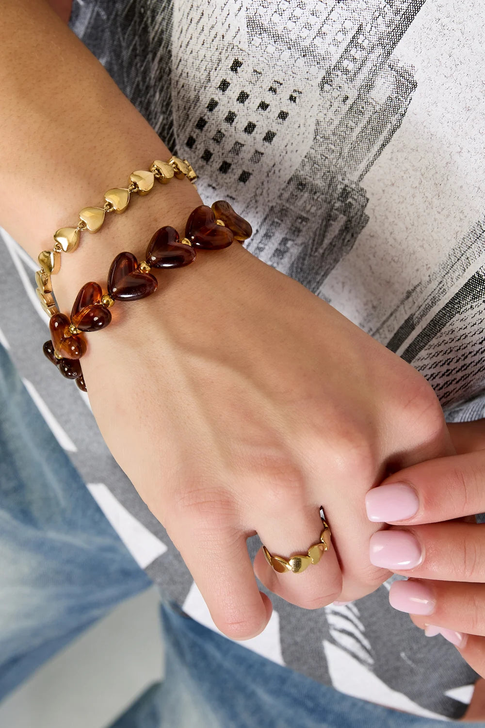 Gestapelde Milena hartjes armbanden van amber en gouden stainless steel om een vrouwenpols, met matchende ring.