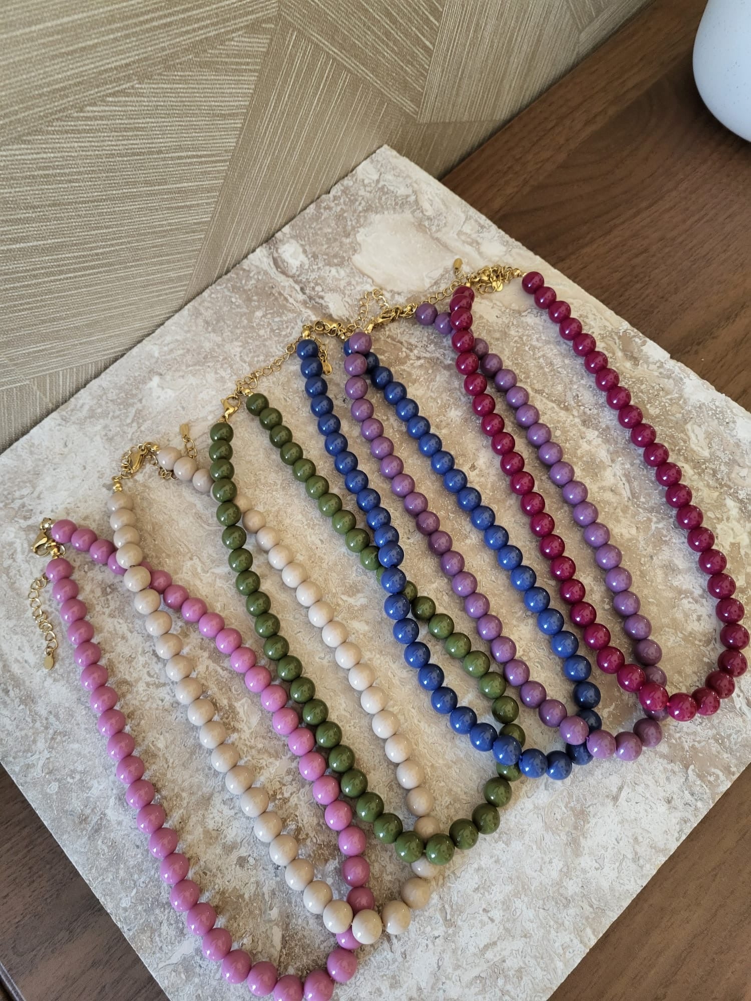Collectie Mira kettingen met paarse, roze, groene, blauwe en crèmekleurige kralen op een stenen ondergrond