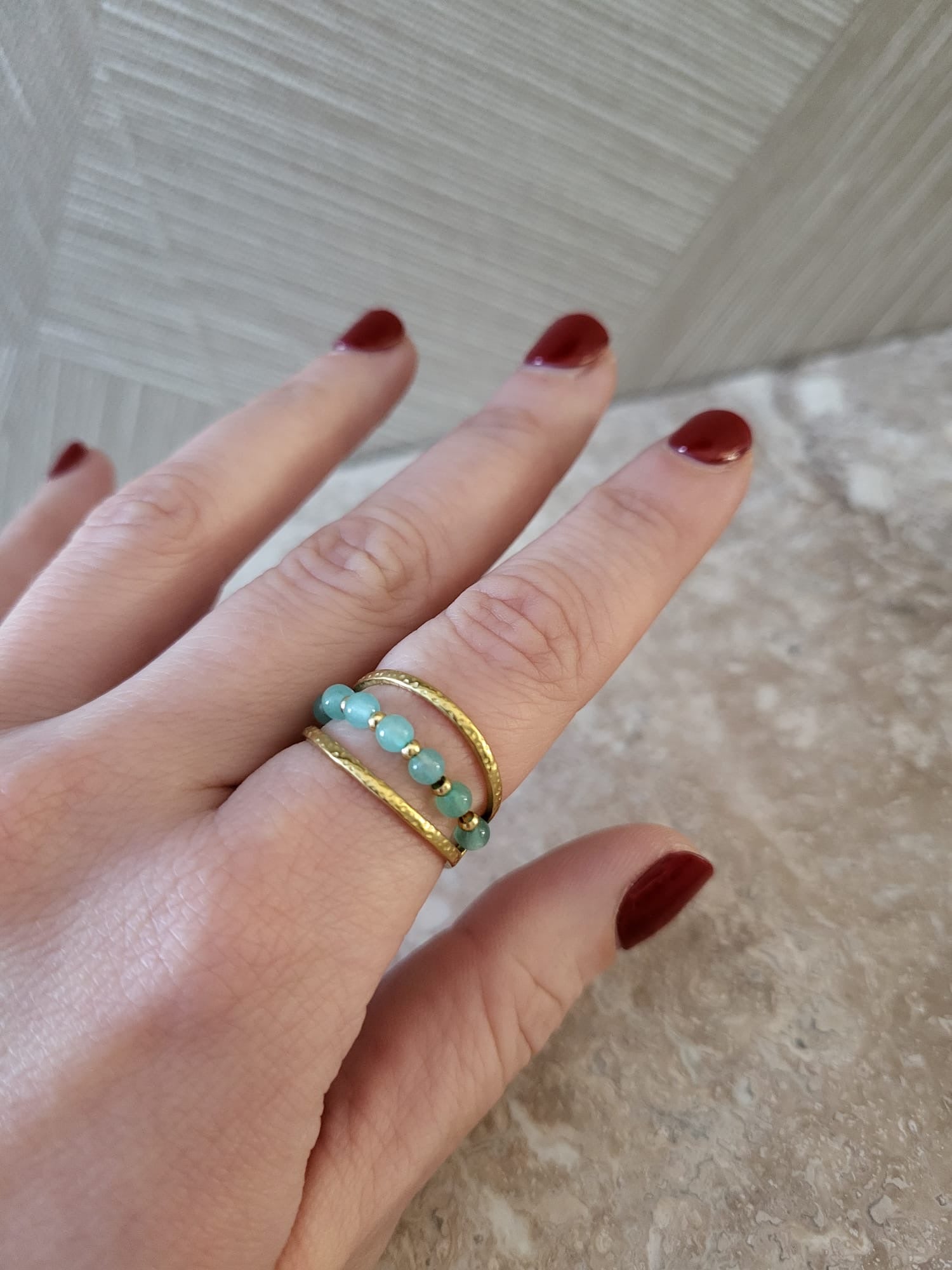 Misty RVS ring met goudkleurige bandjes en turquoise kralen, gedragen aan een vinger met donkerrode nagellak