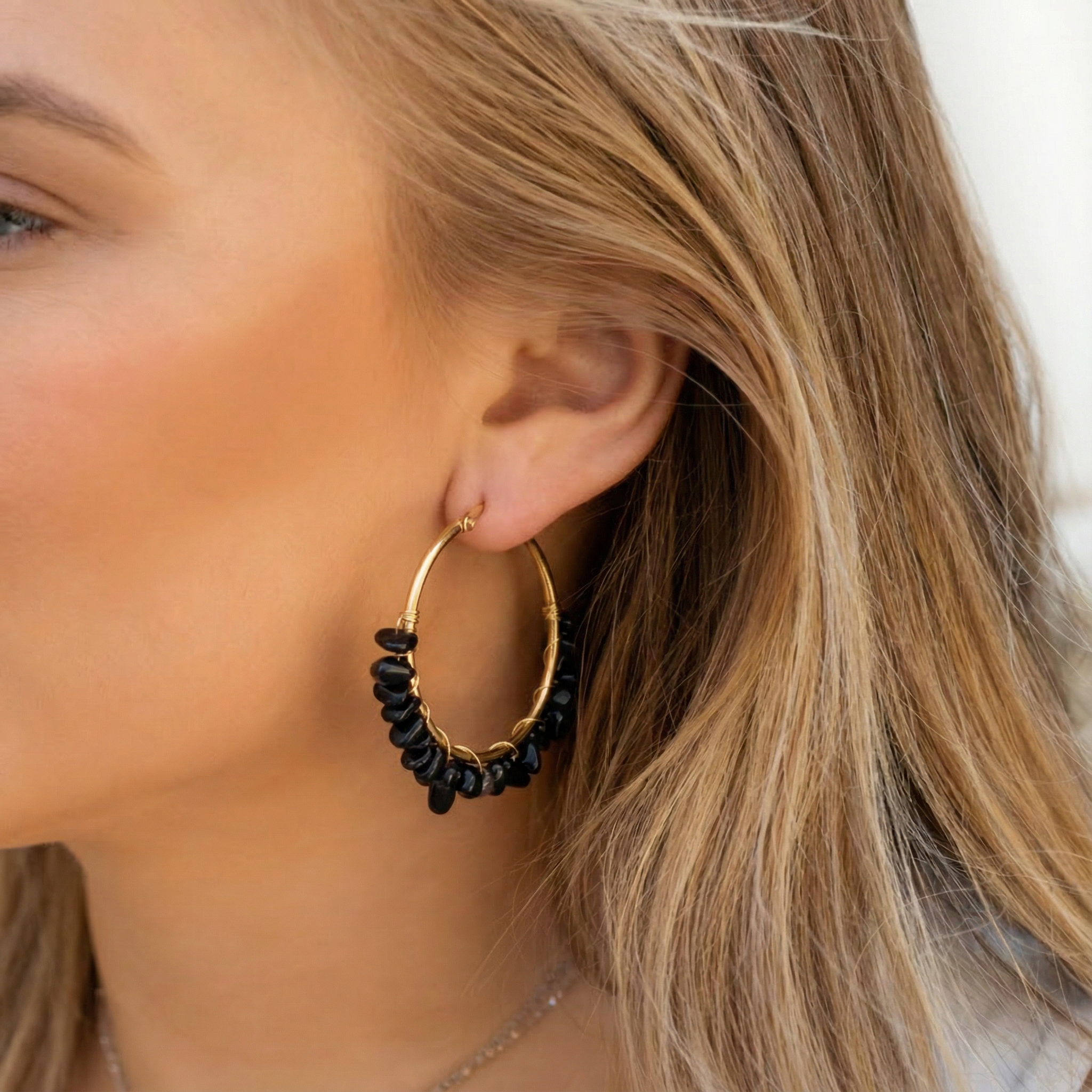 Gouden oorringen met zwarte obsidiaan natuursteen, gedragen door een vrouw. Mooie stainless steel oorbellen.