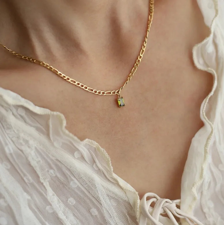 Gouden ketting met rechthoekige groene steen hanger, gemaakt van stainless steel, gedragen op de hals.