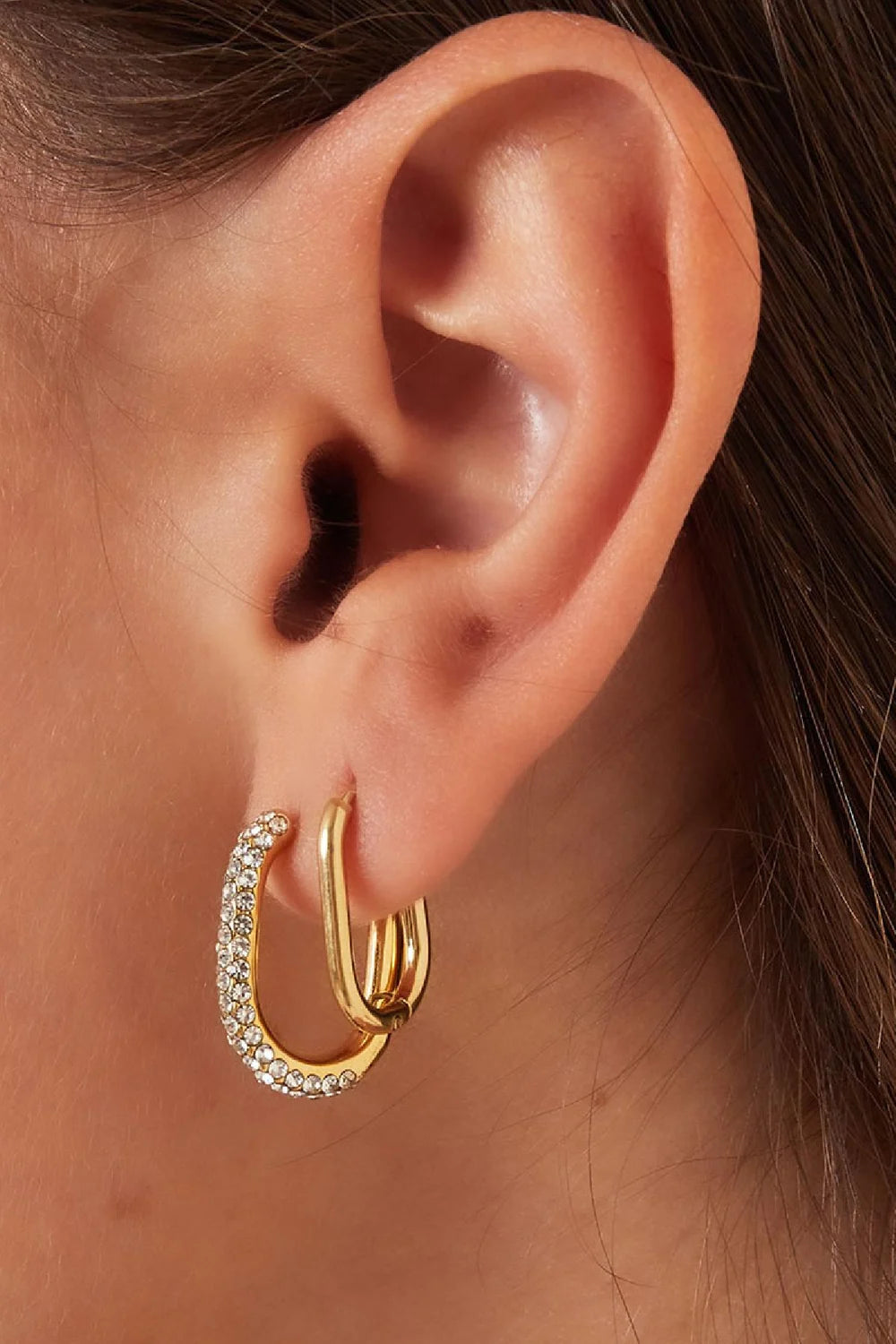 Gouden ovale hoop oorbellen van stainless steel met glinsterende steentjes aan een oor, elegant sieraad