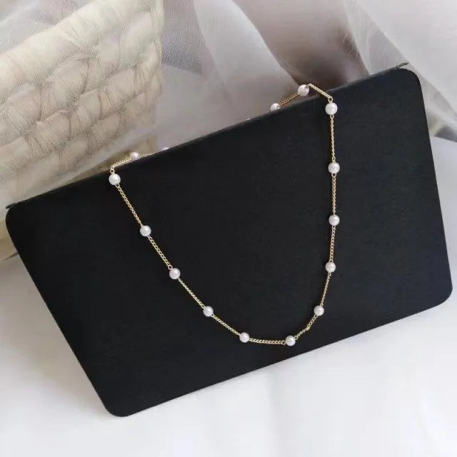 Elegante ketting Petite goudkleurig met kleine, witte imitatie parels op een zwarte ondergrond, fijne sieraden