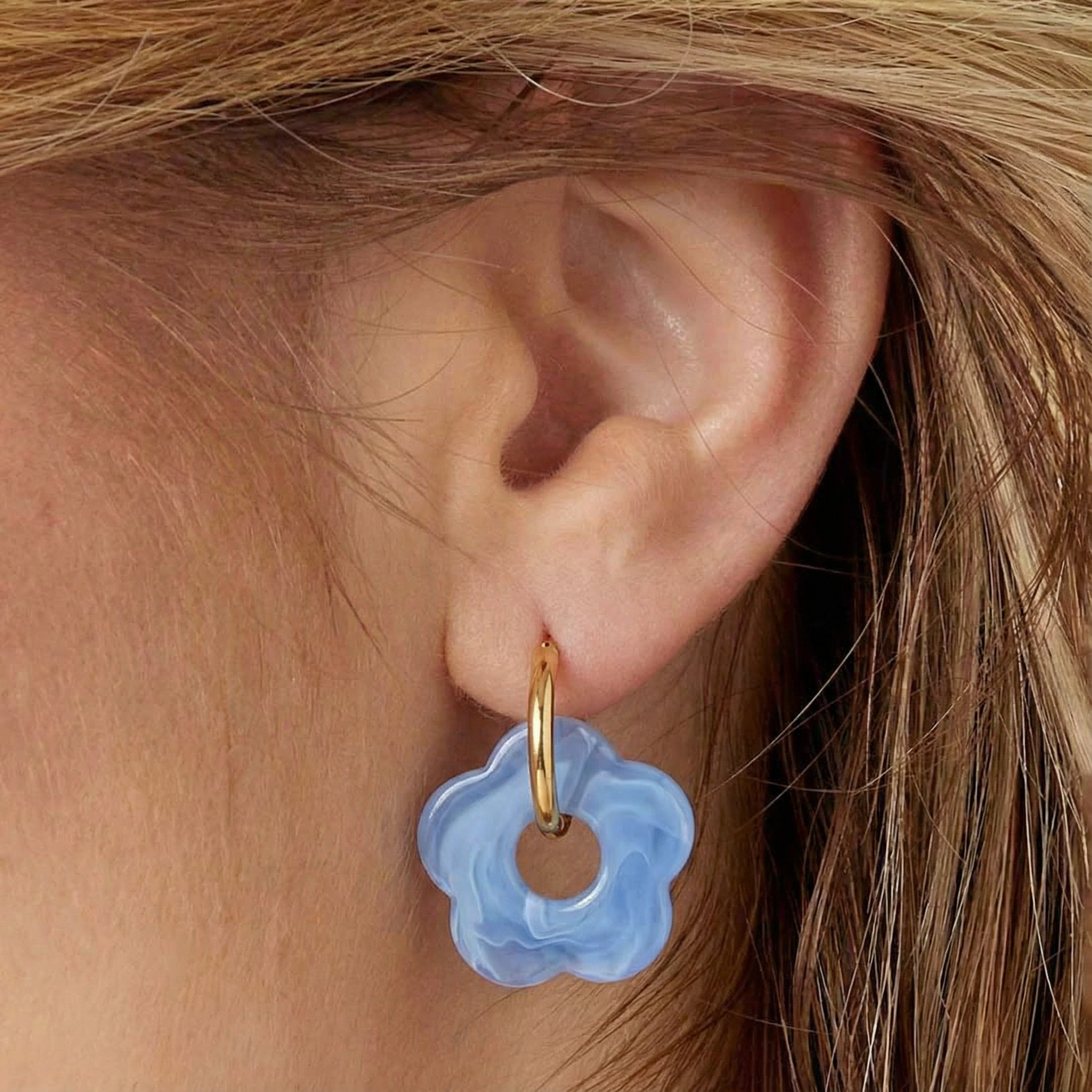 Rosy blauwe bloem oorbellen met goudkleurige ring op een oor, stijlvolle oorbellen met bloem design