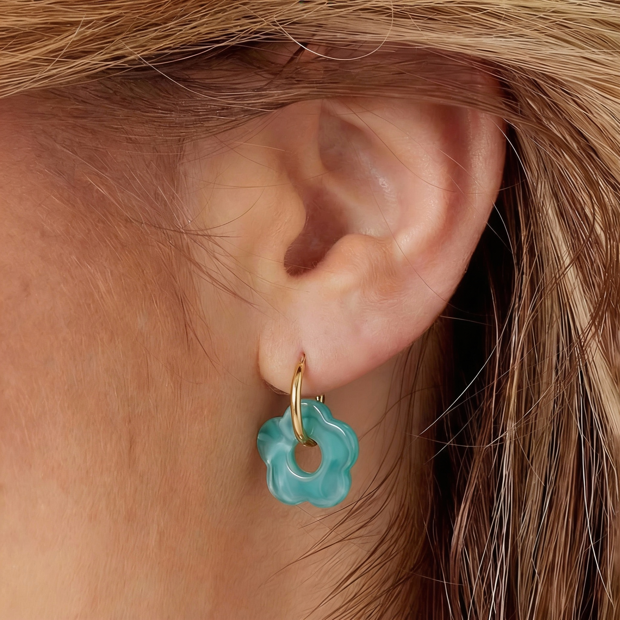 Gouden Rosy oorbellen met bloemvormige, groene hangers van Jewellery by Mae aan het oor van een vrouw.