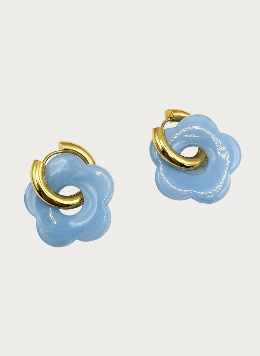 Twee lichtblauwe bloemvormige oorbellen met glanzend gouden oorringen, een speels sieraad.