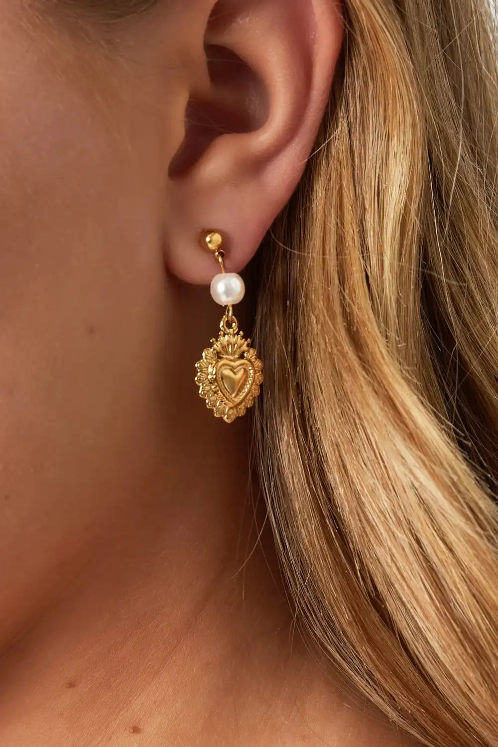 Gouden Royal Heart oorbellen van stainless steel met parel, hangend aan het oor van een blond model.