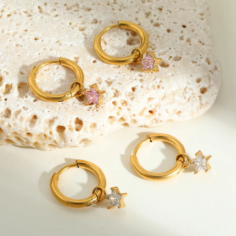 Gouden oorbellen met sterrenhangers. Set van drie paar creolen met roze en witte zirkonia sterren steentjes.