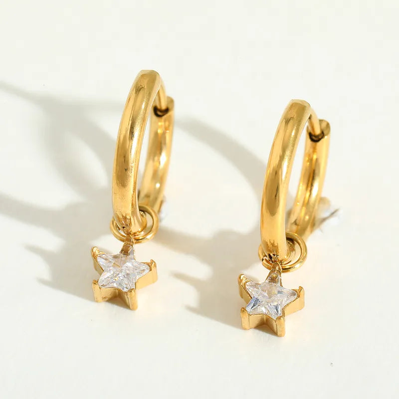 Gouden oorringen met bungelende sterren bezet met witte strass steentjes, glanzende sieraden.