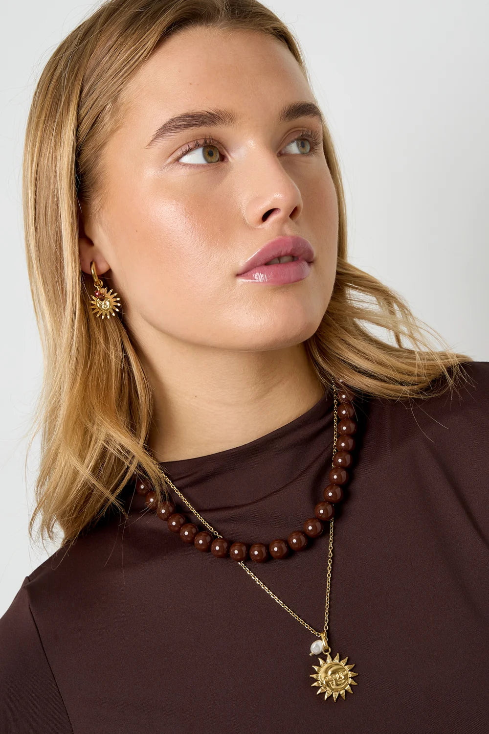 Model met gouden stainless steel ketting met bedel van dubbelzijdige zon en maan en parel, plus bruine kralenketting.