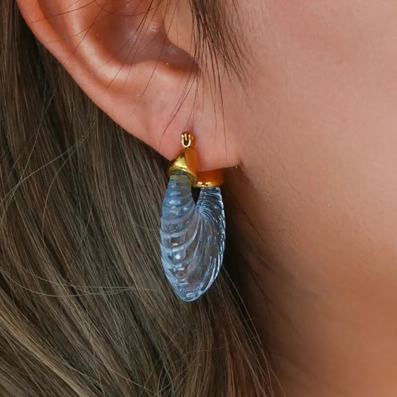 Close-up van oor met blauwe Tamara oorbellen van stainless steel, gegraveerd design, goudkleurige details
