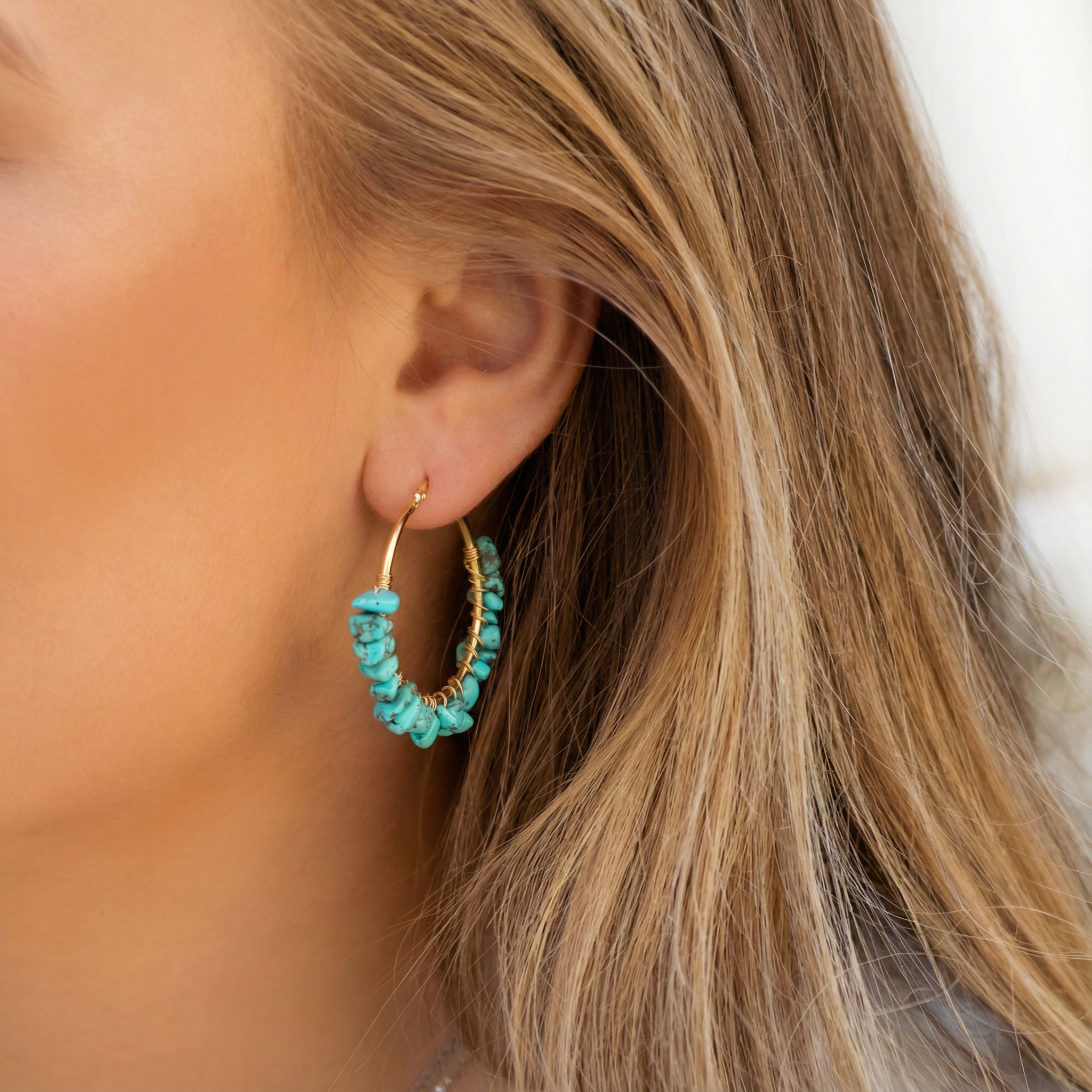 Gouden oorbellen met turquoise natuursteen kralen, gedragen door een vrouw