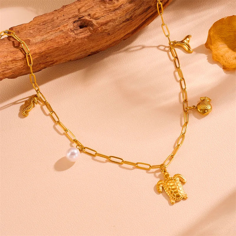 Gouden schakelketting met kleine parel en bedels: schildpad, vis, zeemeerminstaart en schelp, van roestvrij staal